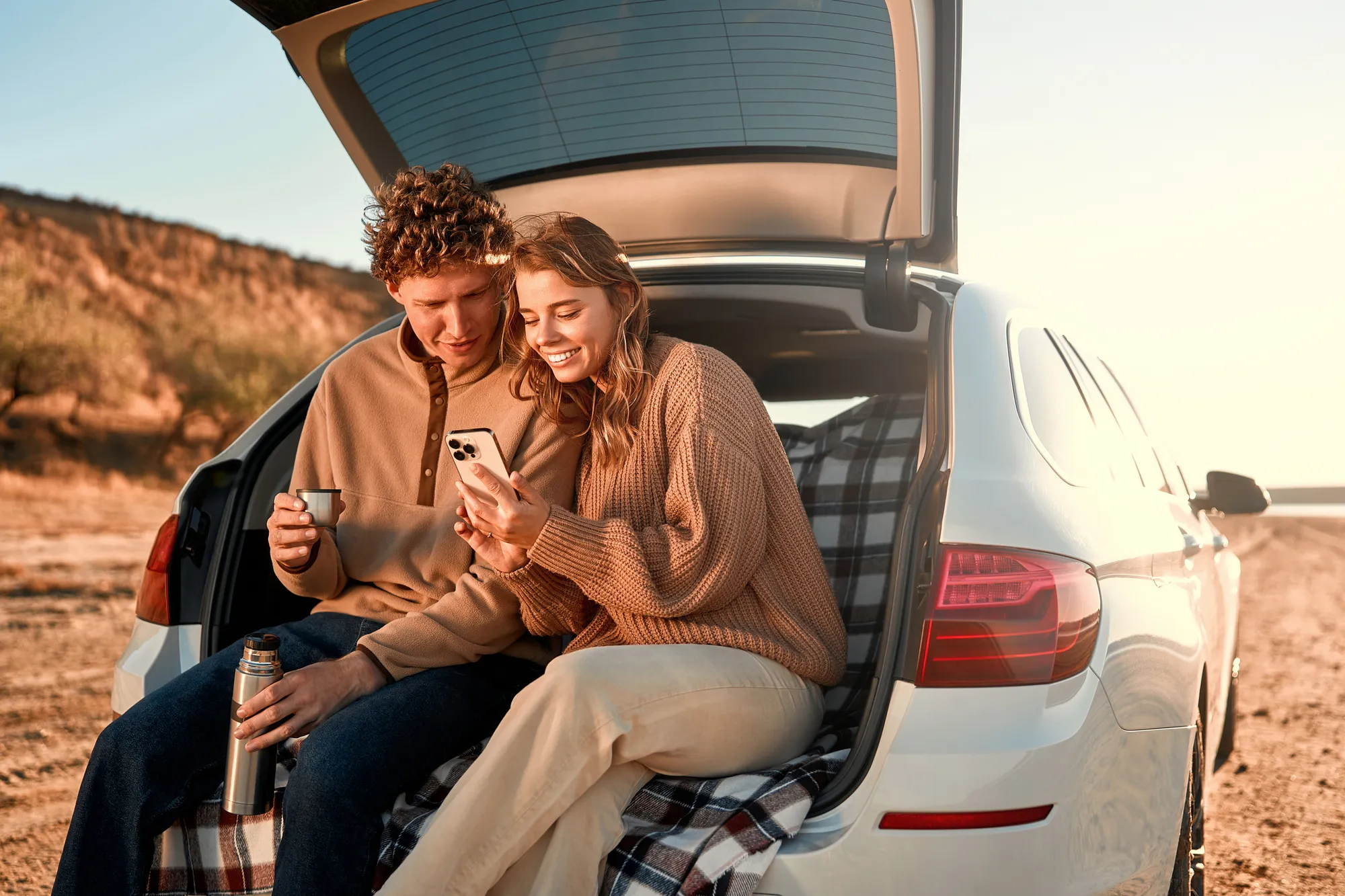 Couple sitting in car trunk looking at phone supporting local fundraiser